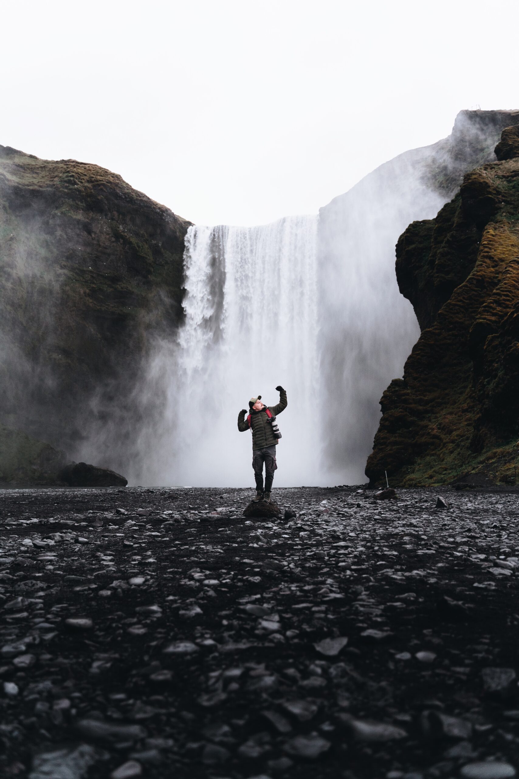 Witness the awe-inspiring beauty of nature as Djordje Vukojicic Photography presents a powerful image of a man standing before a magnificent waterfall.