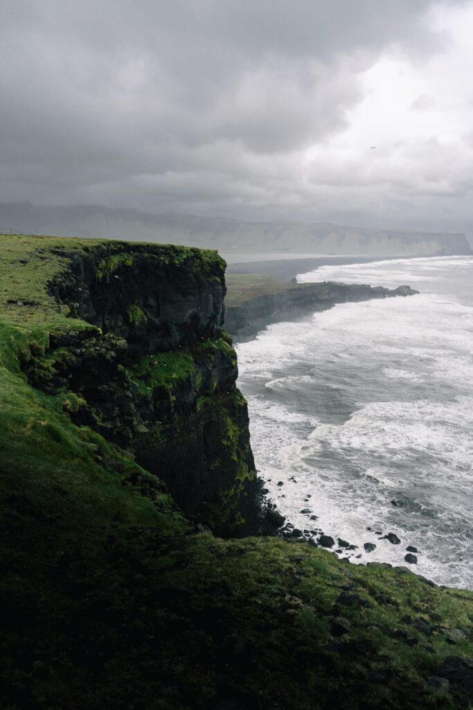  Djordje Vukojicic Photography captures the dramatic beauty of a cliff, framed against a serene body of water, complemented by rugged rock formations.