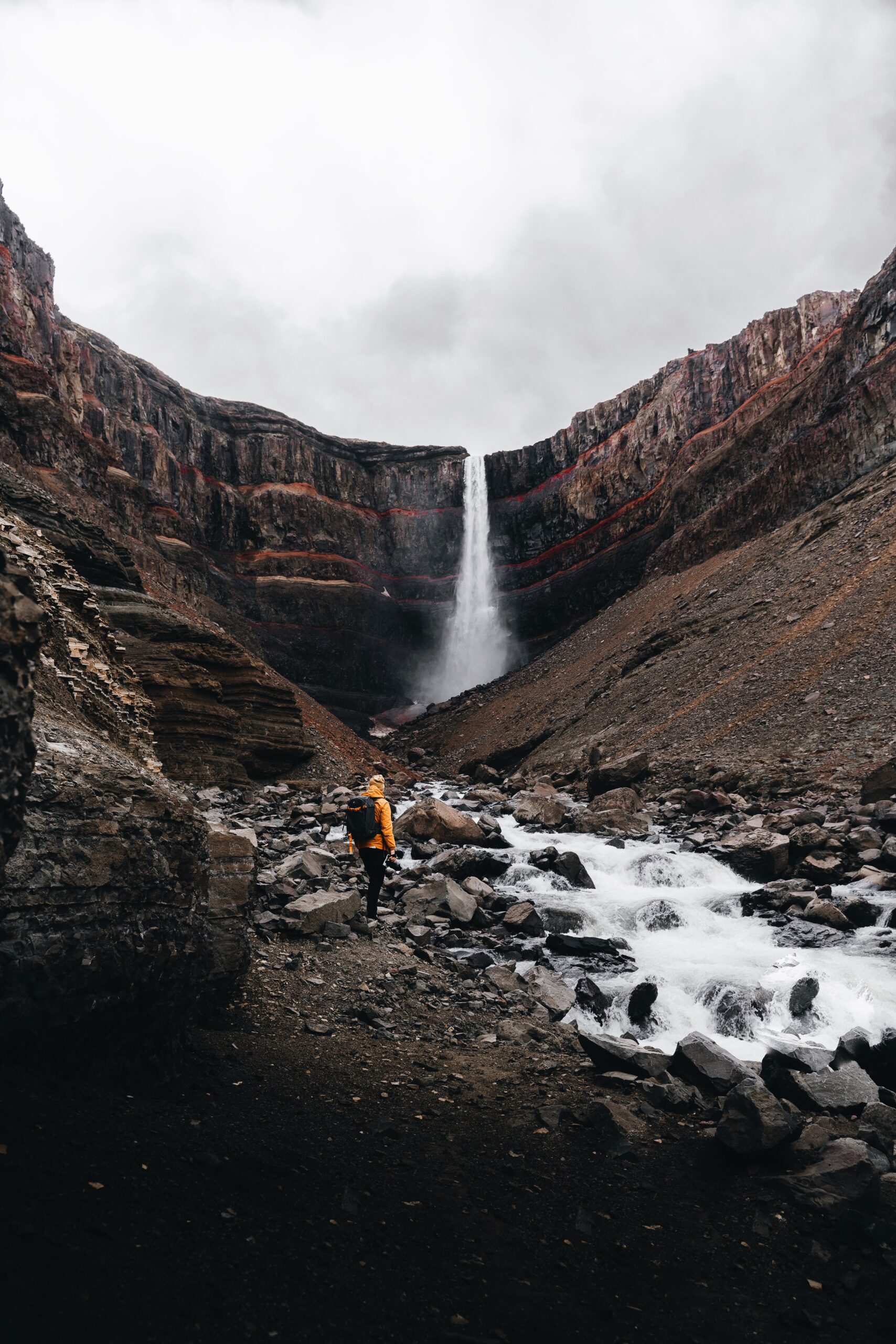 Djordje Vukojicic Photography captures the adventurous spirit amidst nature - a person standing in a rocky canyon, surrounded by the awe-inspiring beauty of a waterfall.