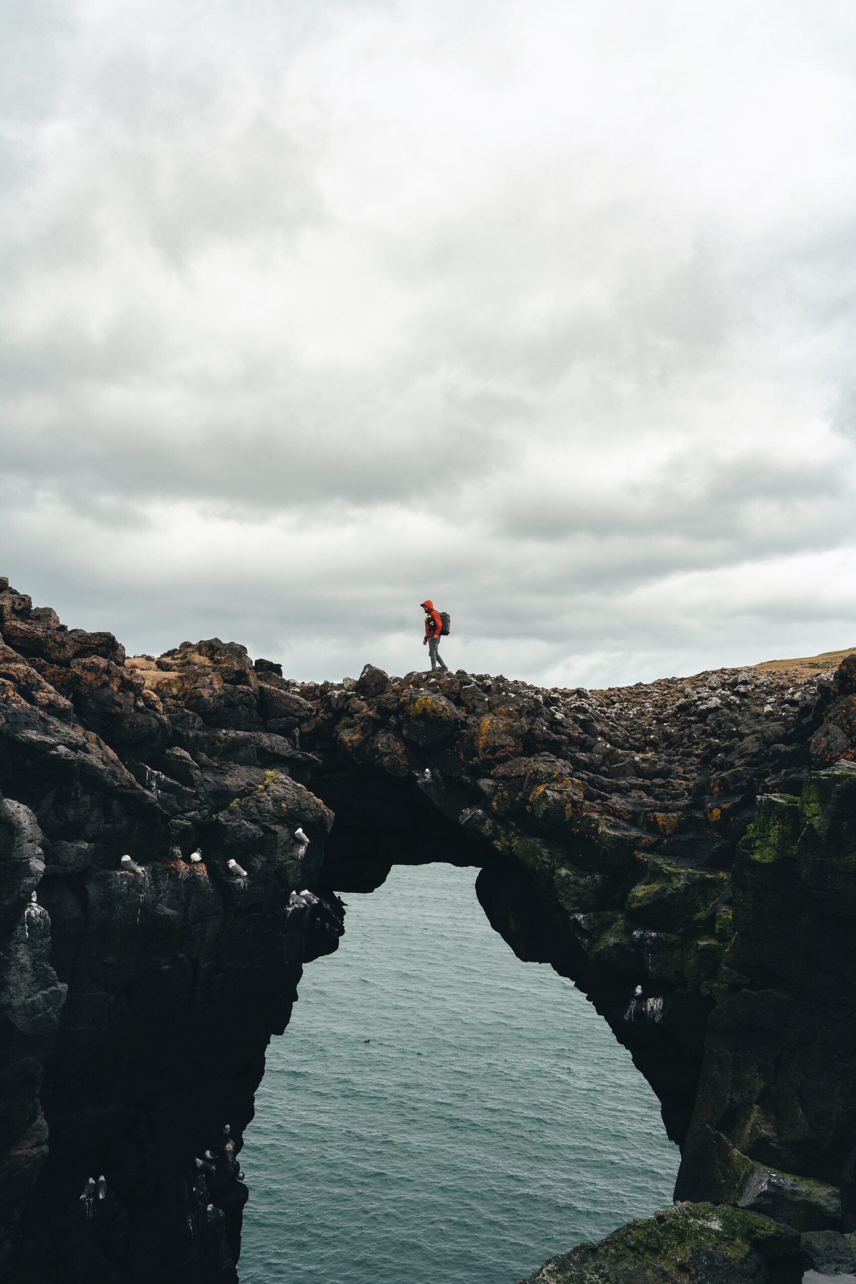  Experience the grandeur of nature with Djordje Vukojicic Photography - a mesmerizing scene of a person standing on a rock arch, framing the vast beauty of the ocean.